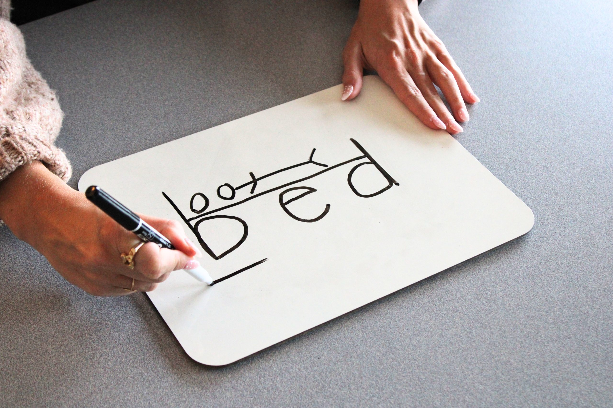 Hand drawing the "bed" trick on a whiteboard, showing how the letters "b" and "d" form the headboard and footboard of a bed