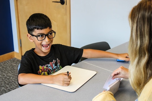 Excited student writing on a whiteboard during a session with his therapist at ETLC