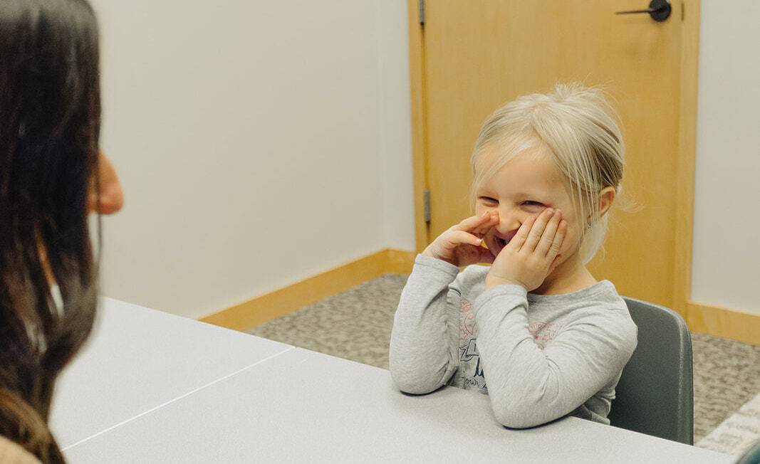 Young girl sitting at a table smiling and covering her face with hands.