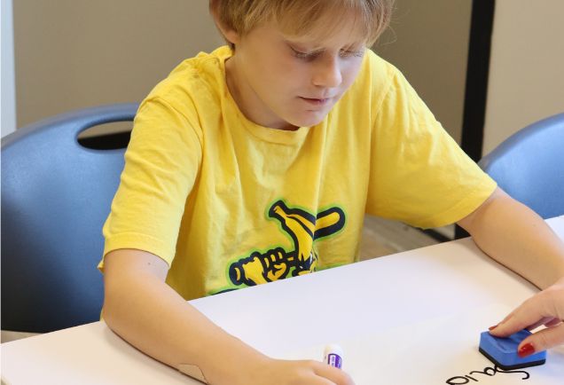 school-ages boy writes in a notebook at a table