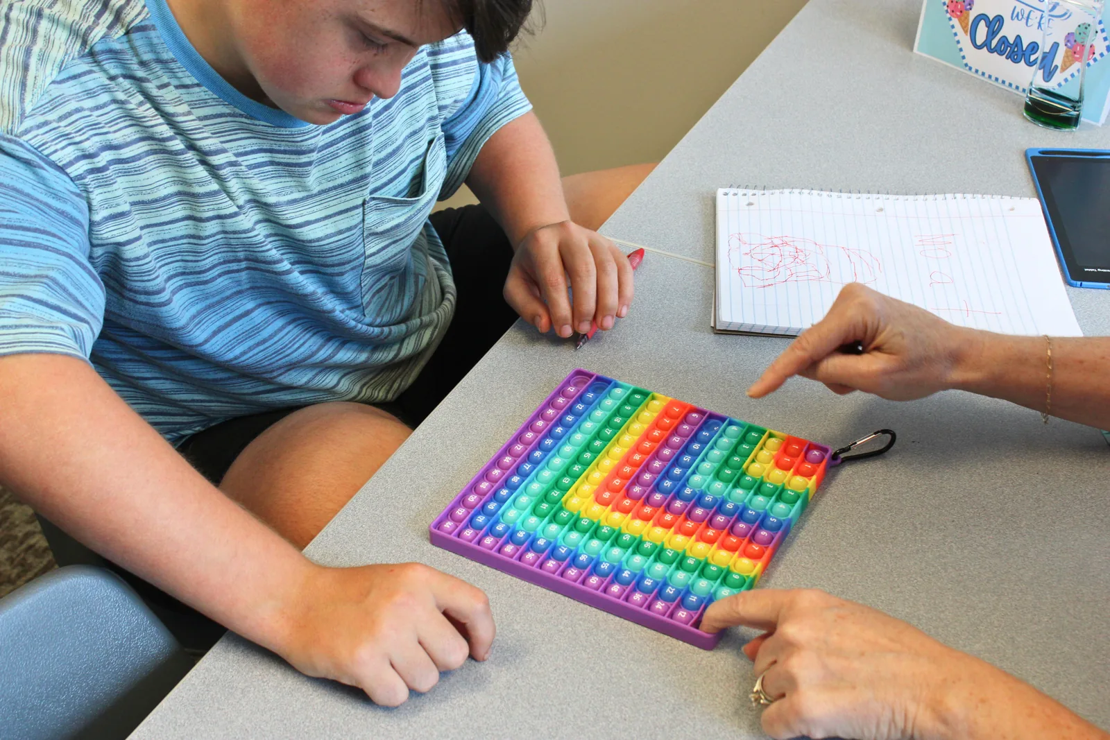 Child and therapist using a colorful hundreds grid to practice math skills at ETLC
