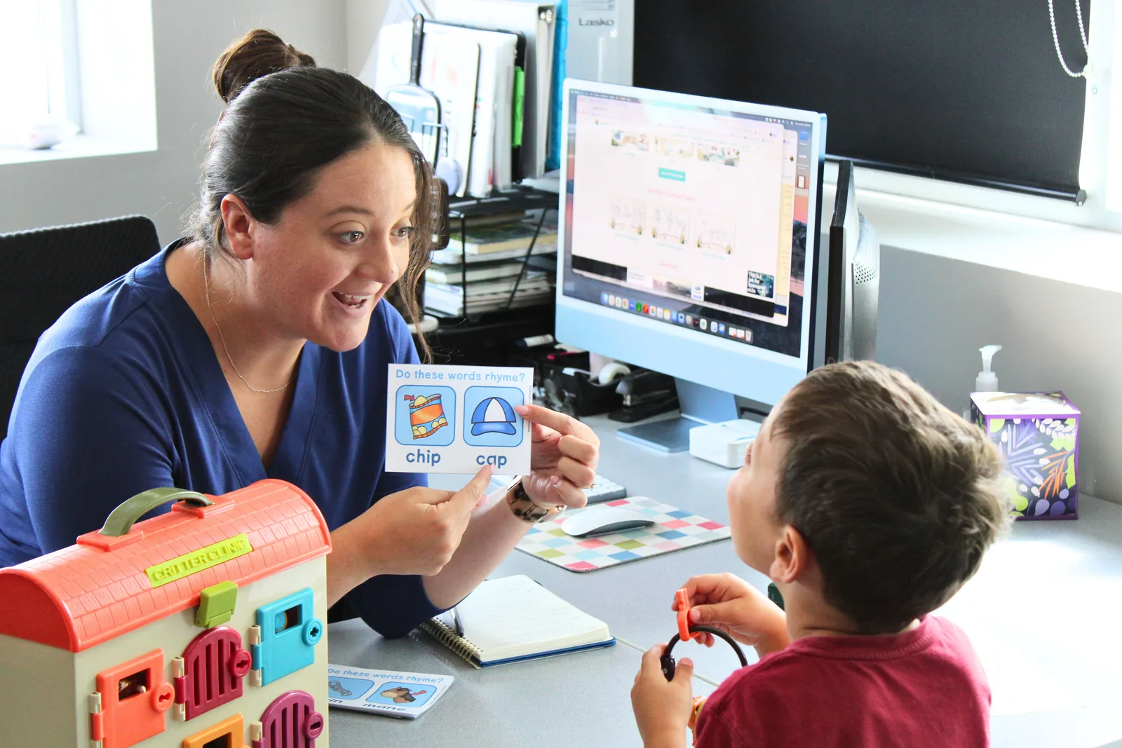 ETLC therapist holding up word cards while a young child practices reading at a desk