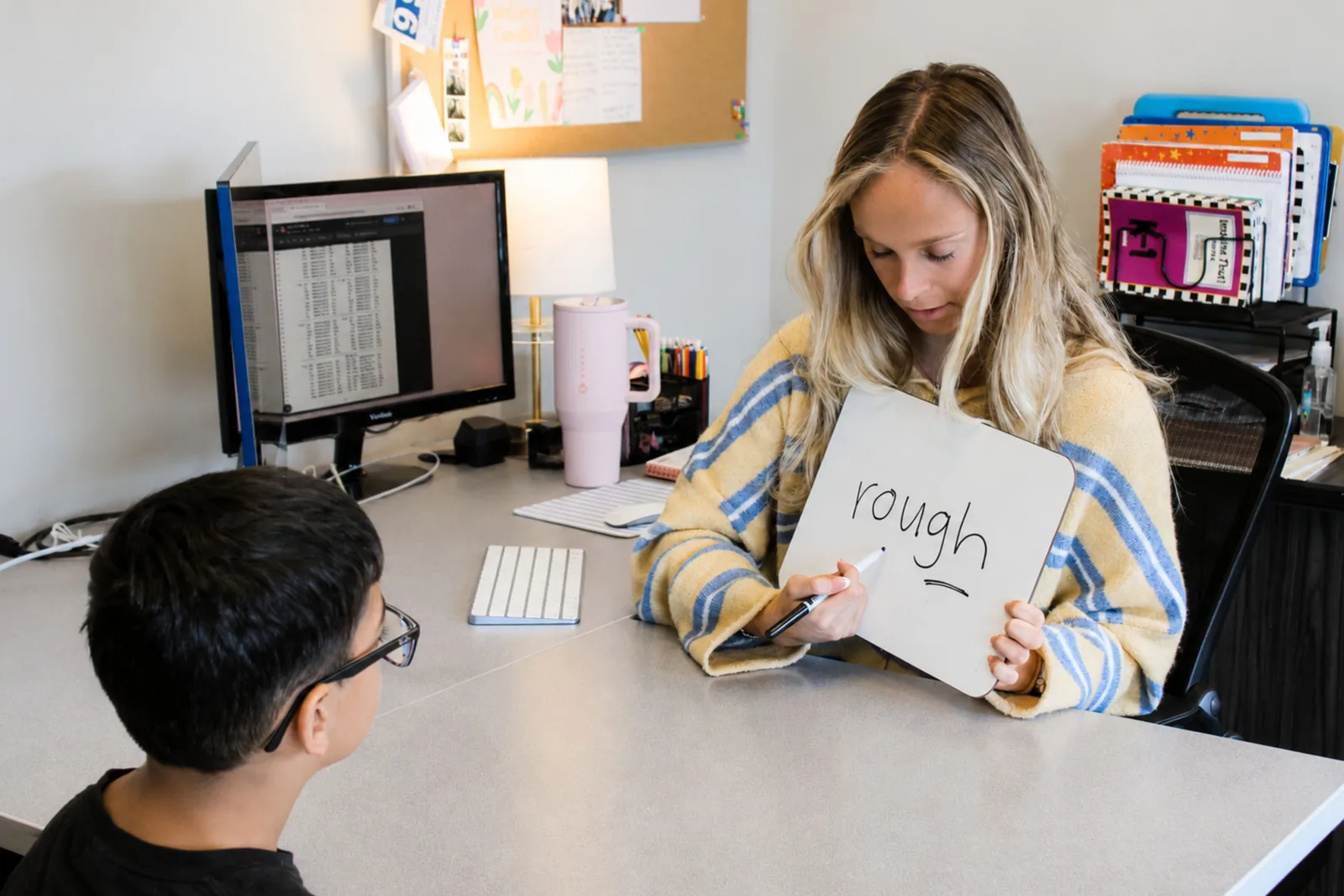 ETLC therapist showing a whiteboard with the word “rough” to a student practicing sight words
