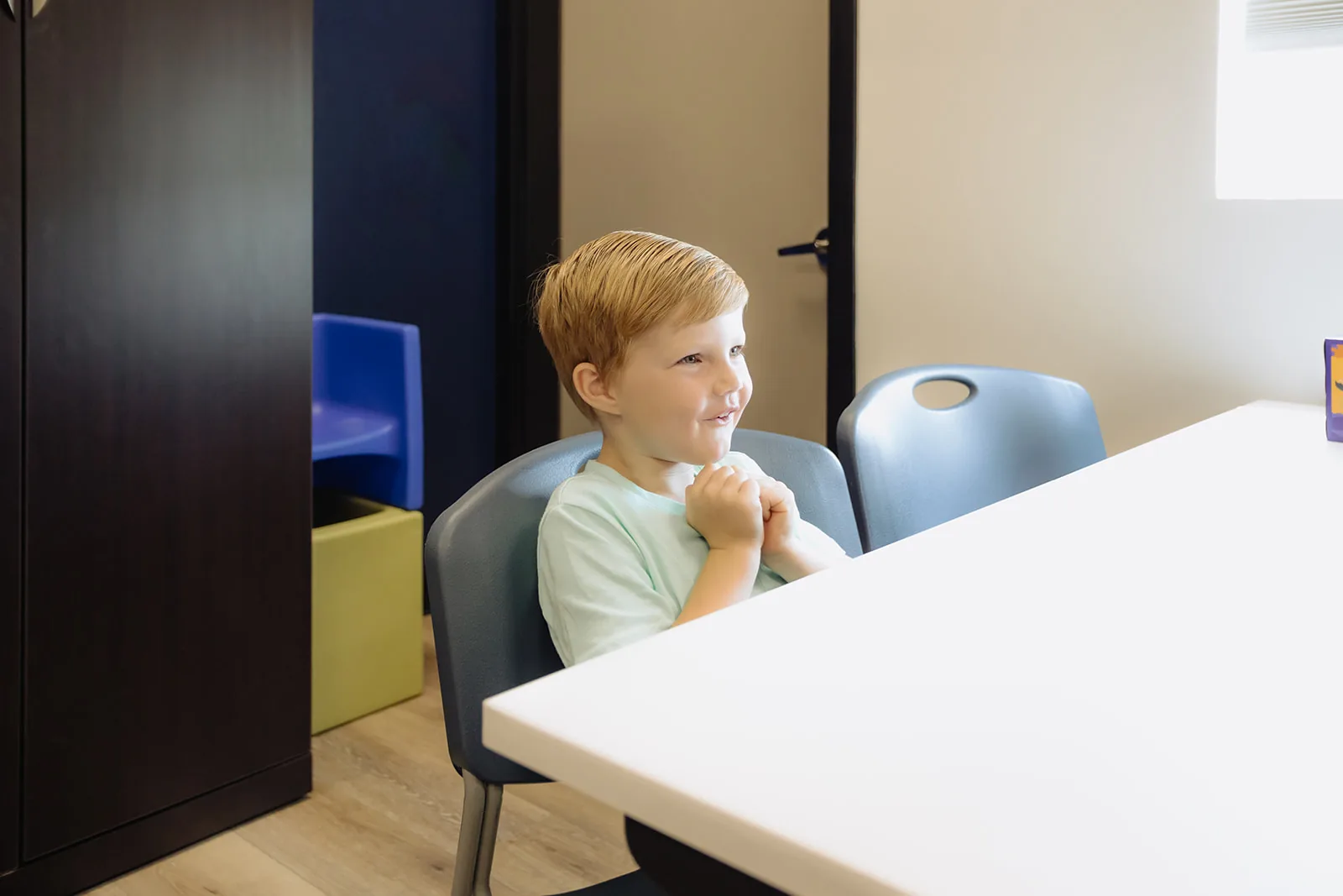 Young boy seated at a table pausing thoughtfully during a fluency therapy session at ETLC