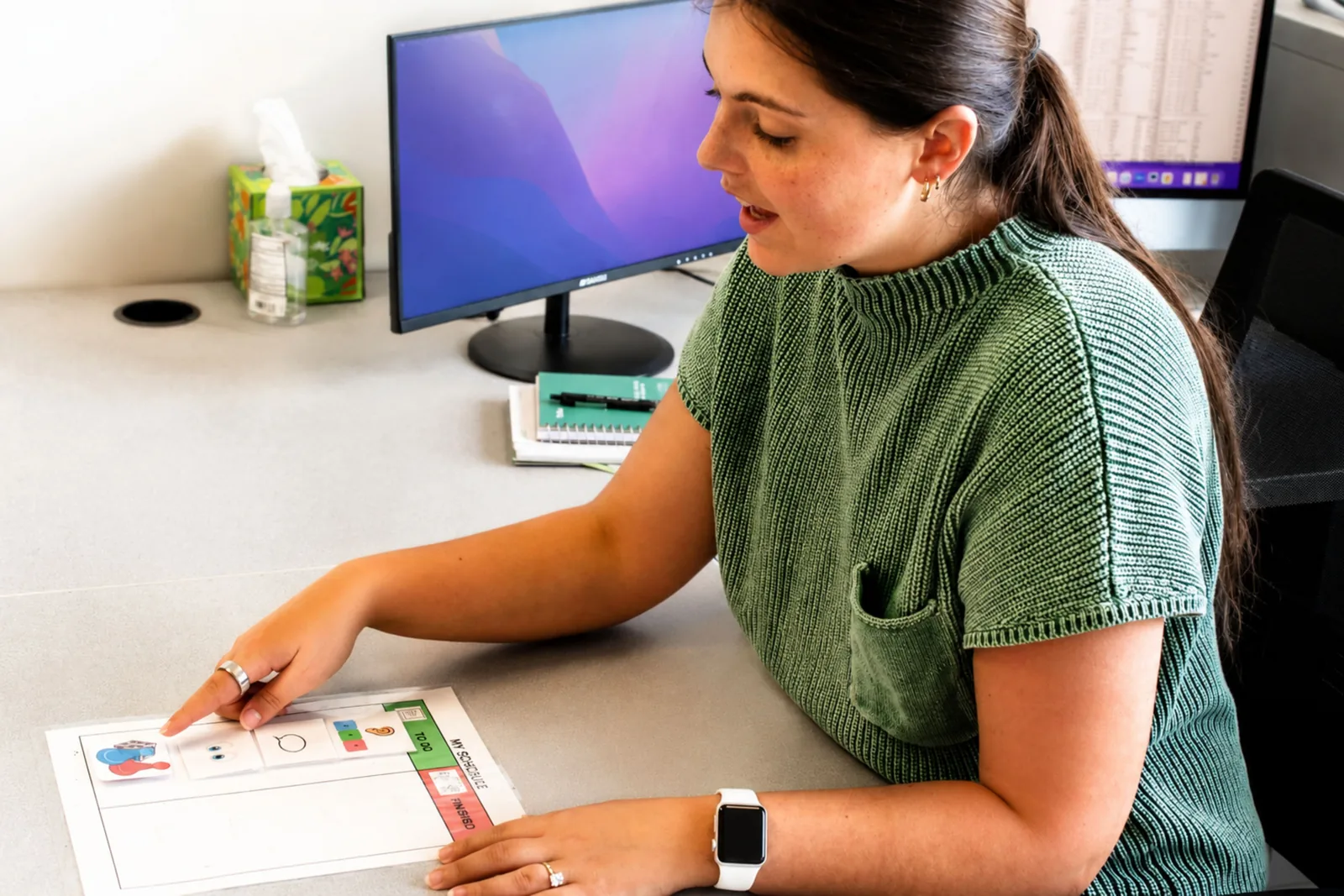 ETLC therapist pointing to a printed visual schedule chart at her desk