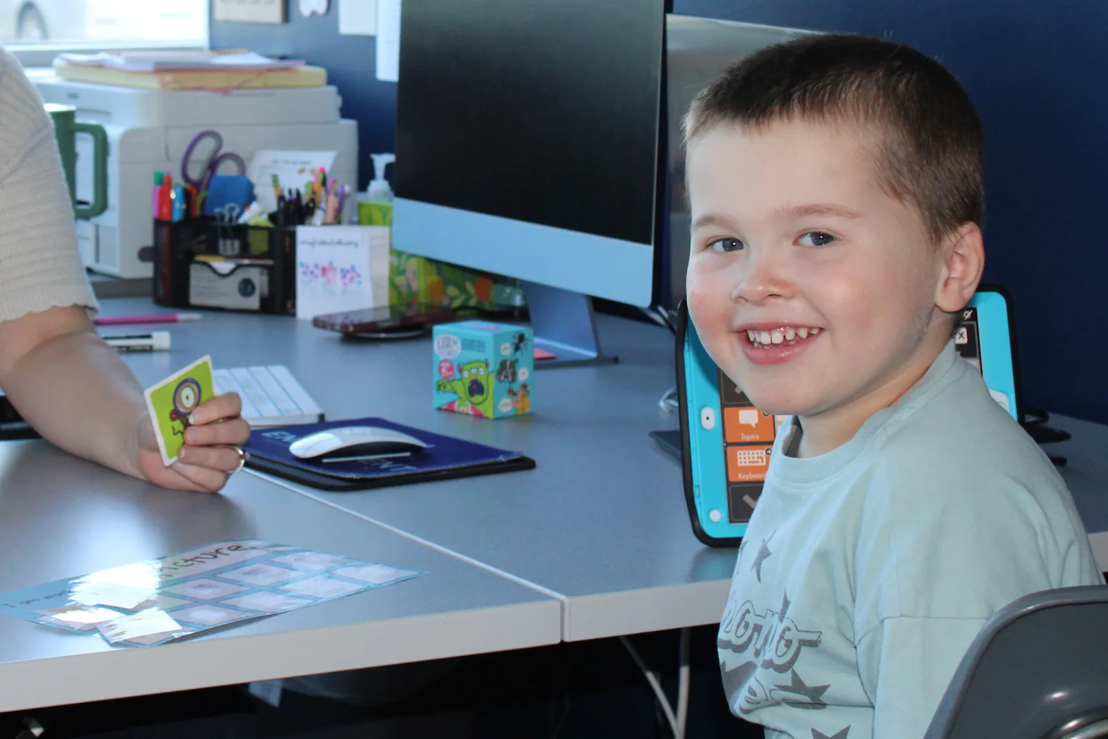 Smiling preschooler at a desk with picture cards during a school readiness screening at ETLC