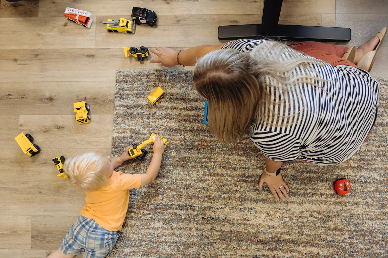 Adult lying on the floor playing with toy cars alongside a toddler during a Floortime session