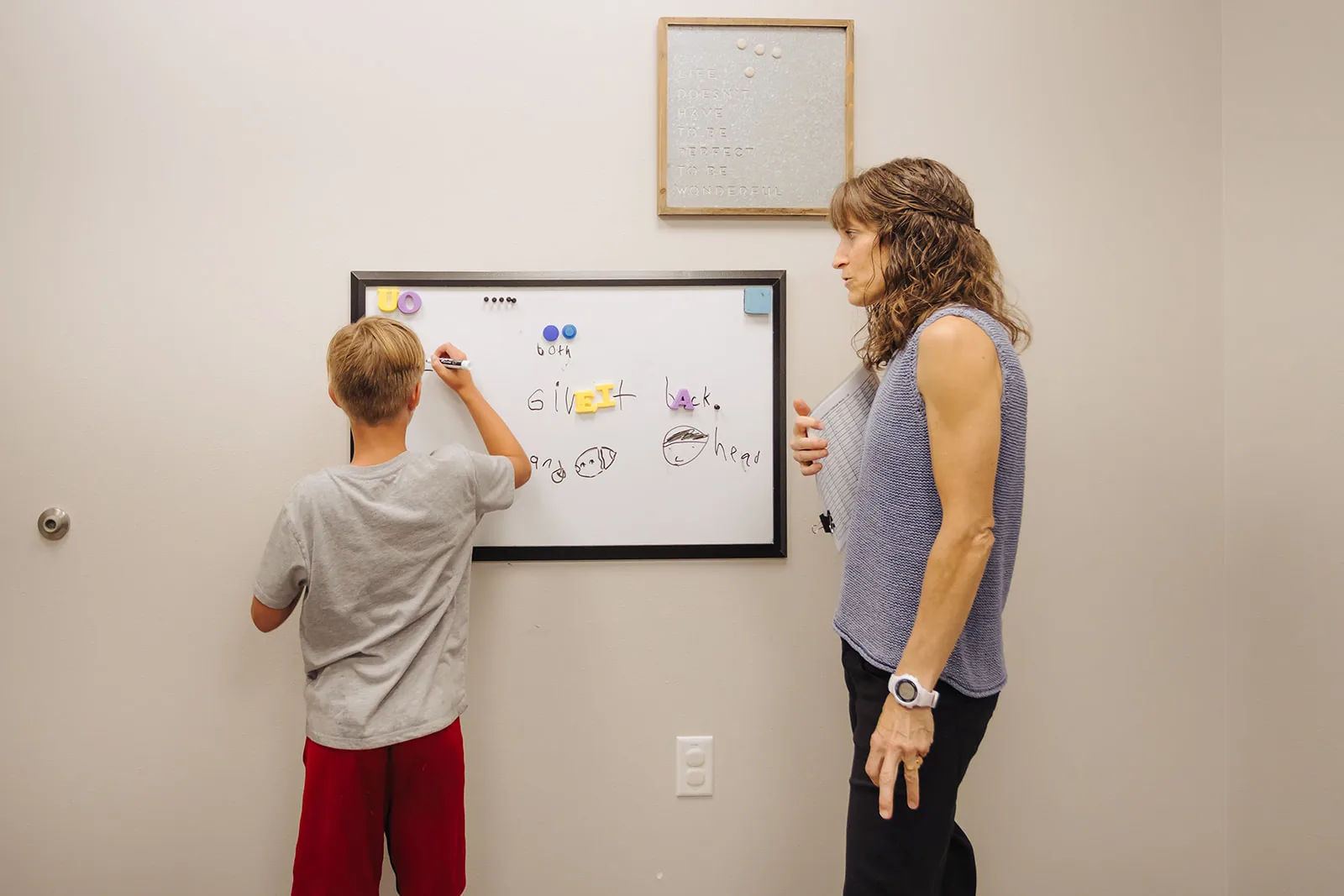 why-is-writing-hard-for-my-child-and-how-can-i-help Boy writing on a whiteboard while an ETLC therapist guides a handwriting activity