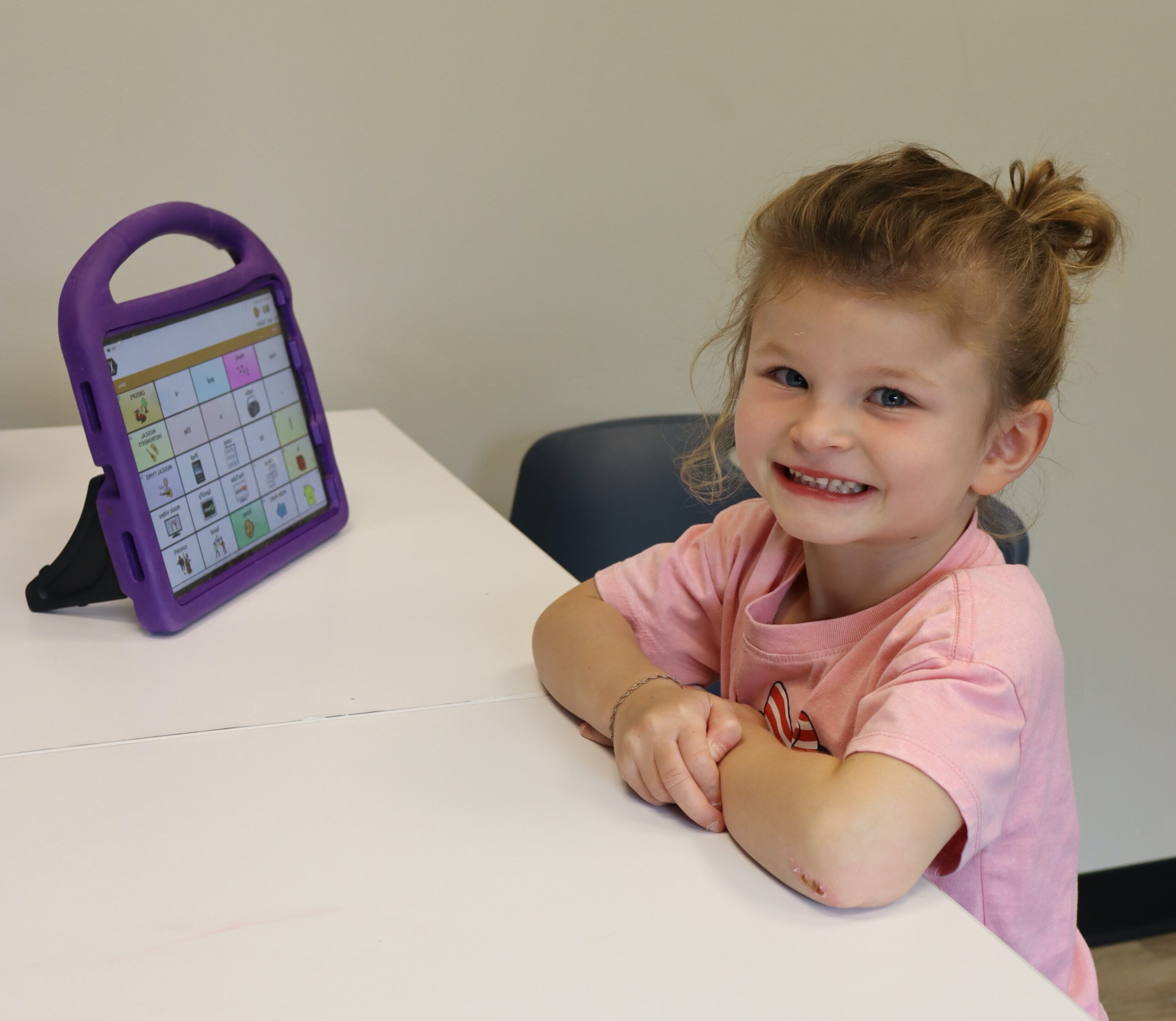Young student smiling while using her AAC device during an early intervention session